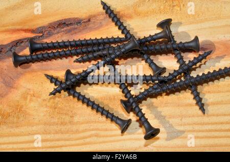 Black colored building screws, displayed on wood background Stock Photo