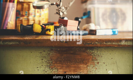 Closeup view of a wooden table used for work, a lot of objects like tools and boxes in blurry background. Stock Photo