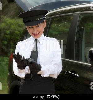 Woman chauffeur wearing a hat and putting on her uniform black leather gloves Stock Photo