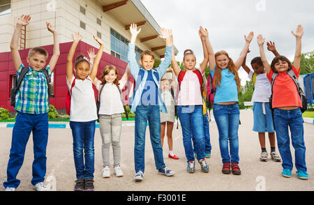Happy children with arms up standing near school Stock Photo