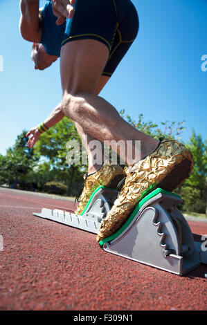 Athlete in gold shoes starting a race from the starting blocks on a red running track Stock Photo