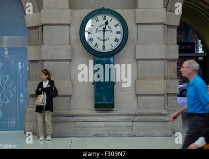 A woman stands and waits under a large old analogue railway clock at Sydney's Central Station in New South Wales, Australia Stock Photo