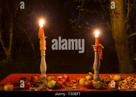 Two candles burn on a table full of apples. Stock Photo