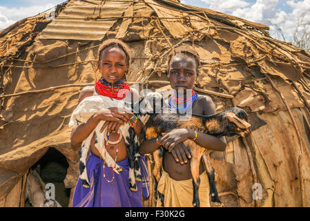 Two girls from the African tribe Daasanach holding goats in front of their home. Stock Photo