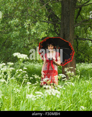 Woman in red dress with black umbrella on walk in park near tree, summer. Stock Photo
