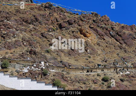 Buddhist prayer flags on the mountain slope and row of buddhist prayer wheels on the outside of the Tashilhunpo monast.-Shigatse Stock Photo