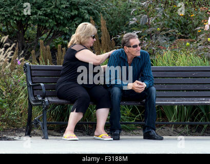 Senior couple man woman sitting on a bench she is scratching his back. Stock Photo