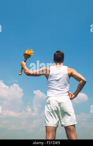 Athlete in old fashioned white uniform holding sport torch against sunny blue sky Stock Photo