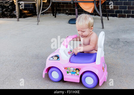 A one year old Caucasian baby girl plays with her riding toy car. USA Stock Photo