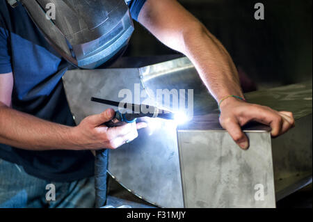 Metalworker welding two metal components with an industrial welder in a workshop, hang angle close up view of his hands Stock Photo