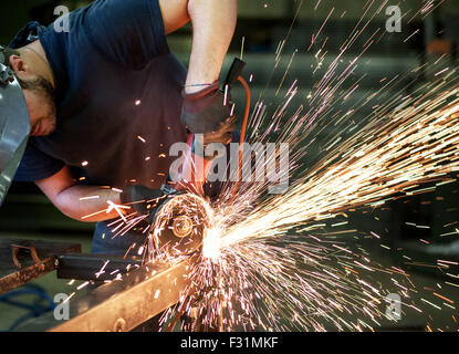 Metalworker cutting a steel bar using a hand held angle grinder power tool Stock Photo