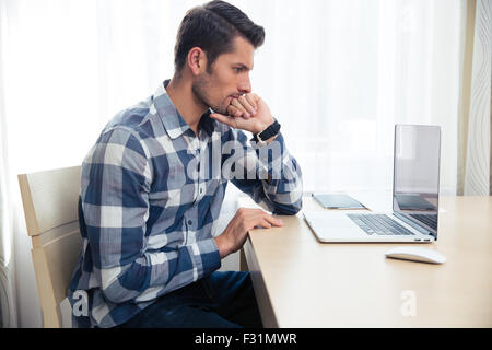 Portrait of a thoughtful man looking on laptop screen at home Stock Photo
