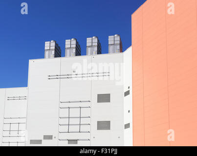Red and white wall of an industrial facility with technical support devices and vent apparatus on the roof Stock Photo