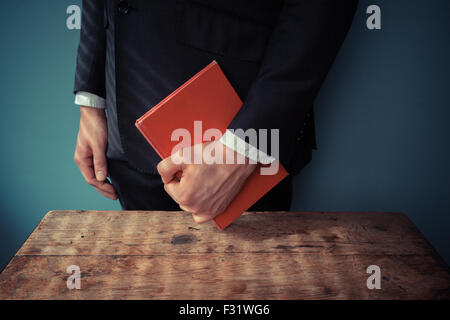 Man standing behind a desk with a red book in his hand Stock Photo