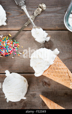 Top view scoop vanilla ice cream in waffle cone with spoon and color rice on wood background. Stock Photo