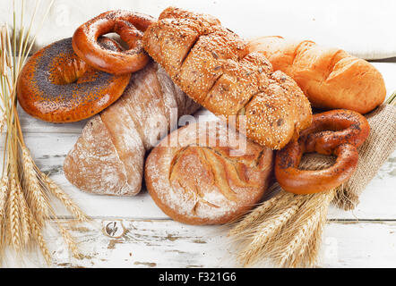 Different fresh bread and wheat on  white wooden table. Stock Photo