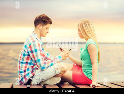 couple with smartphones sitting on bench Stock Photo