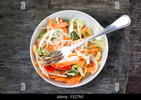 Bowl of salad and fork on a rough wooden background