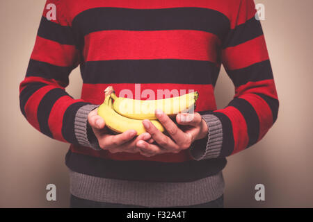 Closeup on a man in a striped jumper holding a bunch of bananas Stock Photo