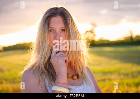A strong backlit portrait of a woman (aged 25 - 30) in a field on a summers evening Stock Photo