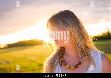A strong backlit portrait of a woman (aged 25 - 30) in a field on a summers evening Stock Photo