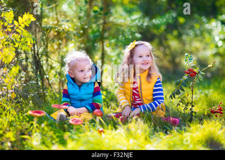 Kids playing in autumn park. Children play outdoors on a sunny fall day. Boy and girl running together hand in hand in a forest. Stock Photo
