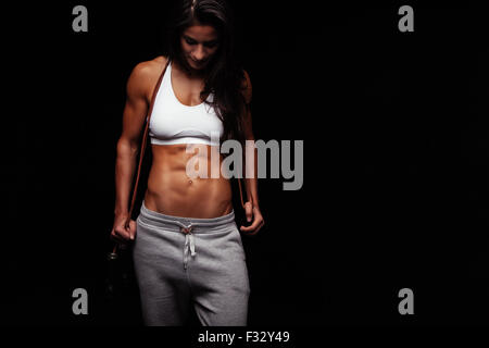 Portrait of muscular young woman with a jumping rope. Female bodybuilder with skipping rope looking down. Stock Photo