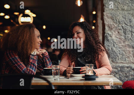 Two women discussing at a restaurant smiling. Young friends sitting in a cafe and talking. Stock Photo