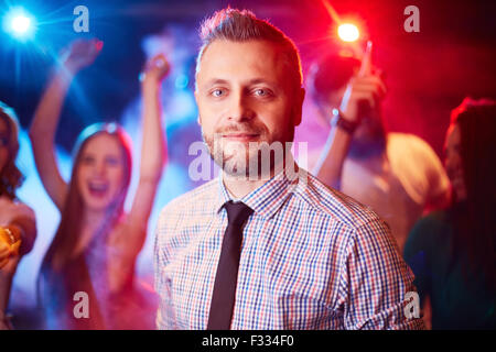 Handsome man looking at camera at party on background of dancing freinds Stock Photo