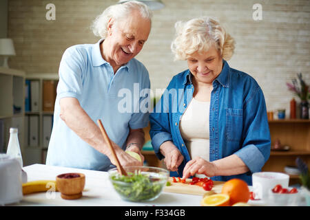 Happy senior couple preparing fresh vegetable salad in the kitchen Stock Photo