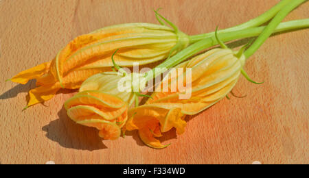 Yellow zucchini blossoms on wooden cutting board Stock Photo