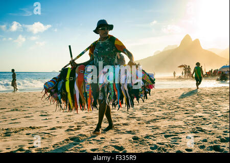 RIO DE JANEIRO, BRAZIL - JANUARY 20, 2013: Vendor selling bikini bathing suits walks on Ipanema Beach during a misty sunset. Stock Photo