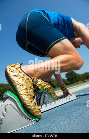 Athlete in gold shoes starting a race from the starting blocks on a blue running track Stock Photo