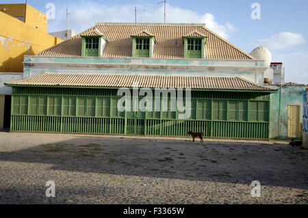 Large, ornate wooden house with long row of green shutters and a dog in front in Boa Vista on the island republic of Cape Verde Stock Photo