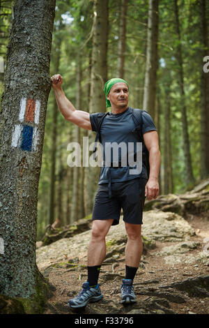 Caucasian man hiker leaning against a tree in a pine forest Stock Photo