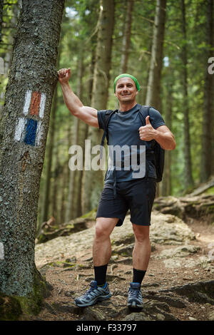 Caucasian hiker with thumbs up leaning against a tree in a pine forest Stock Photo