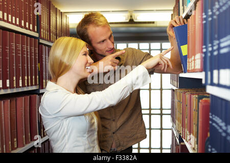 Two students taking books from a shelf Stock Photo