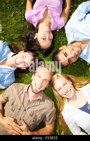 Five happy students lying on green grass Stock Photo