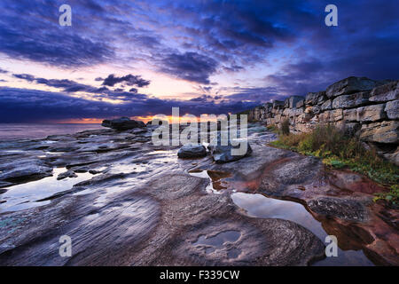 pacific coast in SYdney near Maroubra beach with after rain puddles of water reflecting stormy cloud at sunrise near stone fence Stock Photo