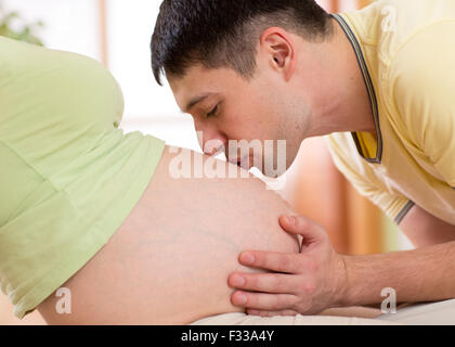 Yong man embraces and kisses a belly of the pregnant woman Stock Photo