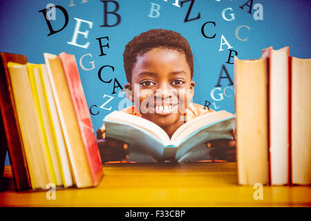 Composite image of cute boy reading book in library Stock Photo