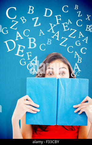 Composite image of portrait of a student hiding behind a blue book Stock Photo