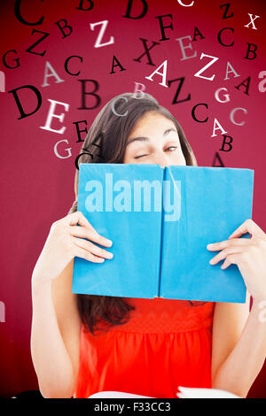 Composite image of portrait of a student winking behind a blue book Stock Photo