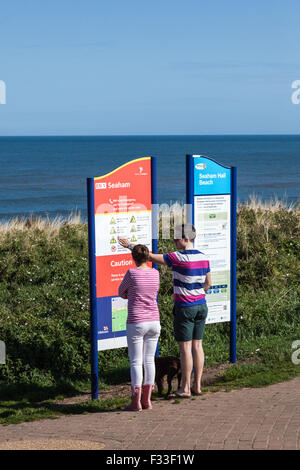 A man and woman couple with a dog look at beach information signs, Seaham, County Durham, UK Stock Photo