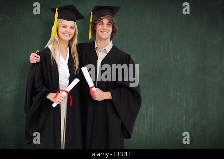 Composite image of two students in graduate robe shoulder to shoulder Stock Photo