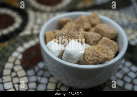 Sugar bowl on mosaic table with raw brown sugar cubes and white cubes Stock Photo