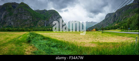 Storm approaching a mountainous valley, farming, agricoltural town in central Norway. Waterfall dropping from the highlands, summer snowmelt. Crops. Stock Photo