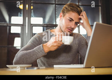 Overworked man drinking coffee and looking at laptop Stock Photo