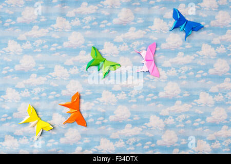 Colourful Origami paper butterflies on a cloudy sky pattern background Stock Photo
