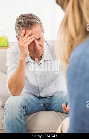 Worried man sitting on couch and talking to therapist Stock Photo